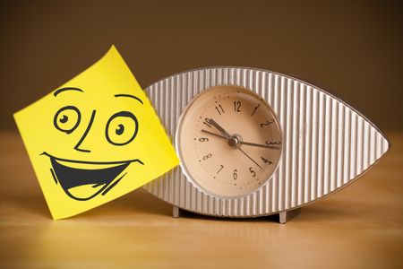 Drawn smiley face on a post-it note sticked on a clock