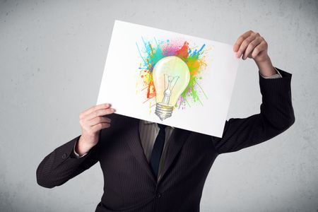 Businessman holding a cardboard with coloured paint splashes and lightbulb in front of his head