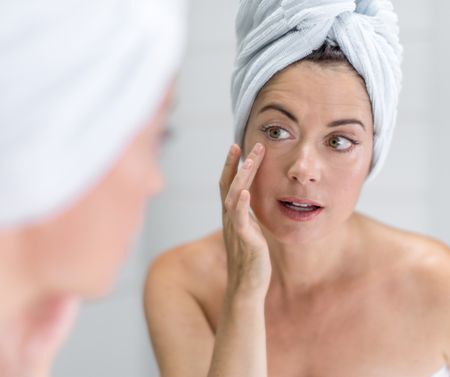 portrait of a beautiful mature lady with a towel on her head looking at her skin in the mirror