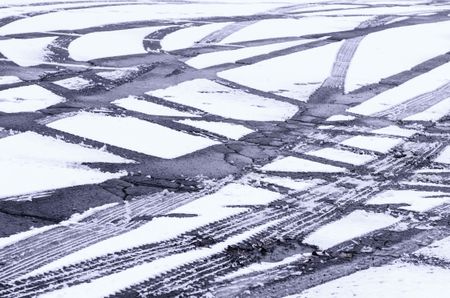 Winter at a glance: Fresh tire tracks intersecting in light snow on asphalt pavement of parking lot