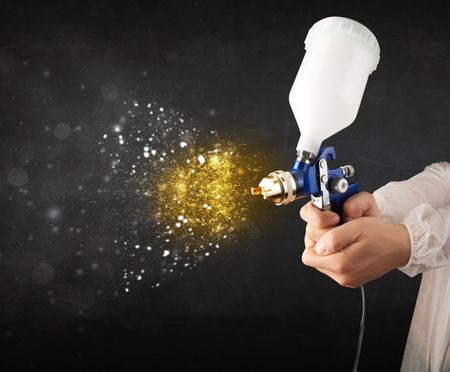 Worker with airbrush painting with glowing golden paint and particles