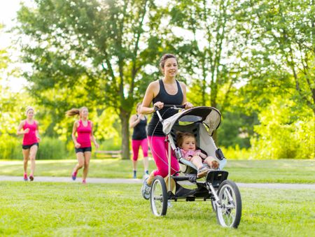 Woman pushing her little girl in a toddler while running outside with friends