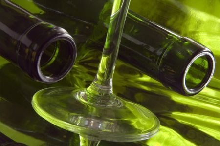 Necks of two wine bottles by base and stem of one wine glass on reflective surface
