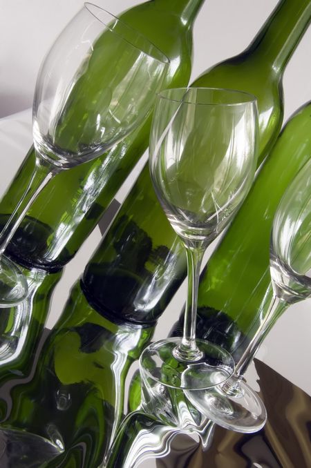 Three wine glasses, one tilted, by three wine bottles on reflective surface