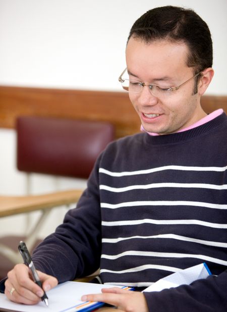 man studying in a classroom - smiling and writting on his notebook