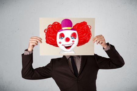 Young businessman holding a cardboard with a clown on it in front of his head