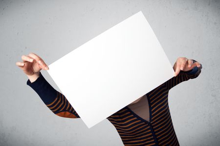 Woman standing and holding in front of her head a white paper with copy space