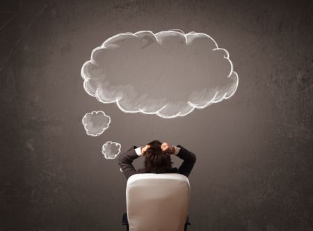 Young businessman sitting in office chair in front of a wall with cloud thought sketched on a chalkboard above his head