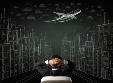 Young businessman sitting in an office chair and looking on a sketched cityscape drawing on a chalkboard