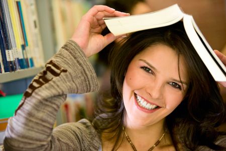 beautiful female student looking happy and smiling with a book in his head in the library