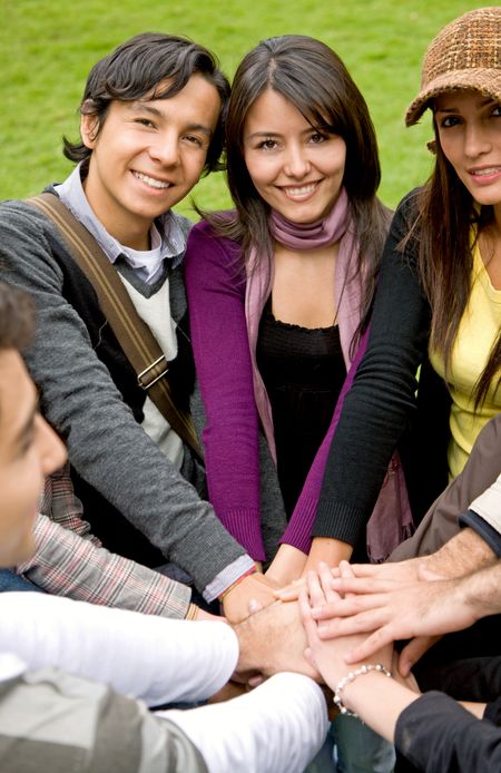 happy group of friends smiling outdoors in a park with their hands together