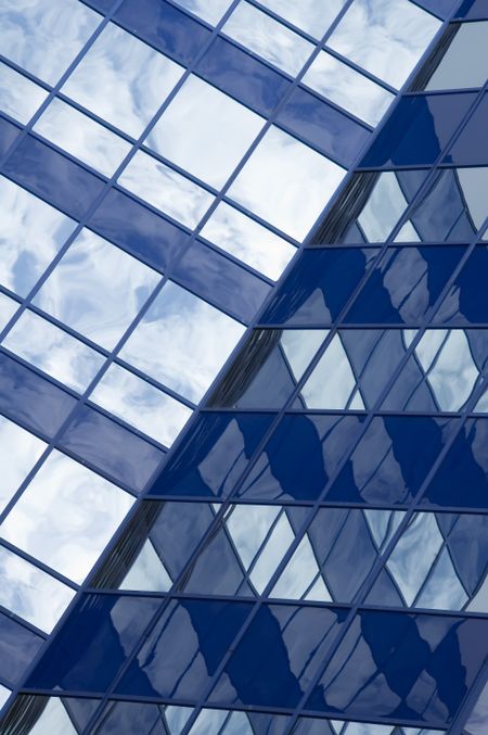 Intersection of two skyscraper walls that reflect a cloudy sky