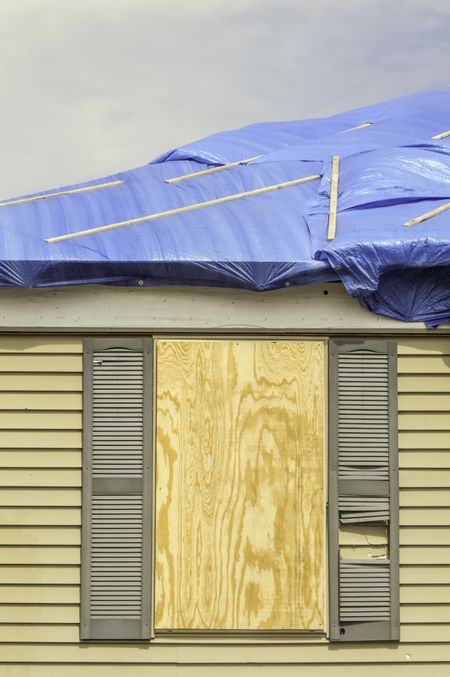 House repairs after tornado: Boarded window beneath roof with protective sheets of blue plastic