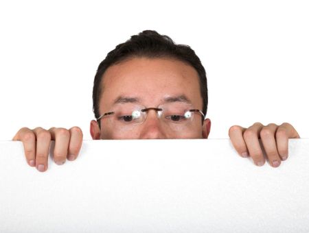 man with glasses peeping over white card over white background