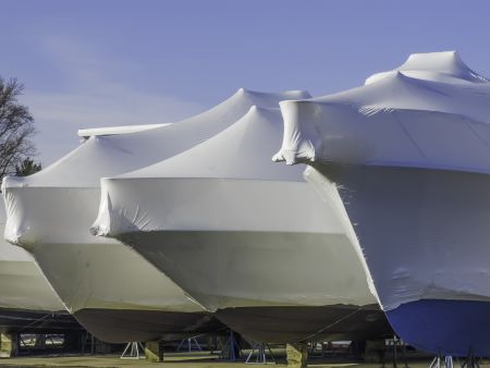 Waiting for nice weather is part of a lifestyle: Bows of shrink-wrapped yachts in boatyard on a sunny morning, spring in southwestern Michigan