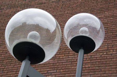 Two big outdoor lights with reflective globes before red brick wall