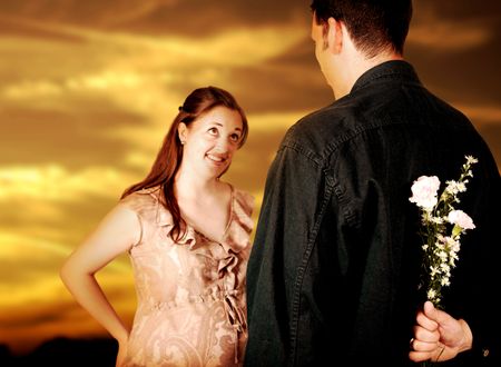 couple at sunset - guy hiding flowers - focus on flowers