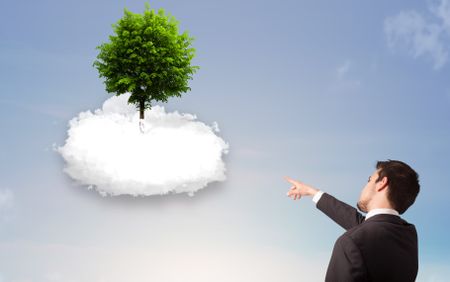 Young man pointing at a green tree on top of a white cloud concept