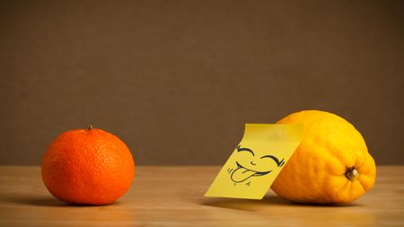 Lemon with sticky post-it note gesturing with tongue to orange