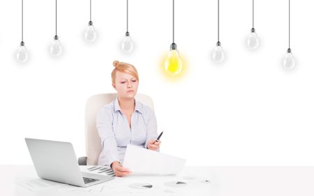 Business woman sitting at table with bright idea light bulbs