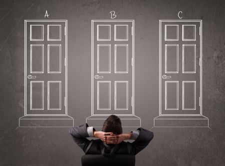 Young businessman sitting in front of a chalkboard and trying to choose the right door