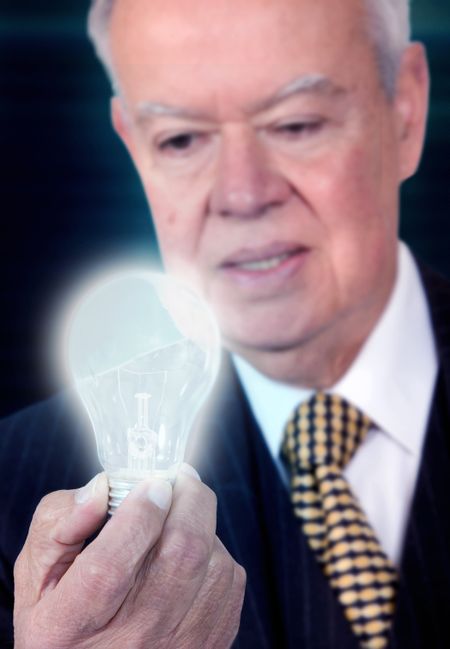 business senior with a lightbulb thinking of ideas for his business over a dark background
