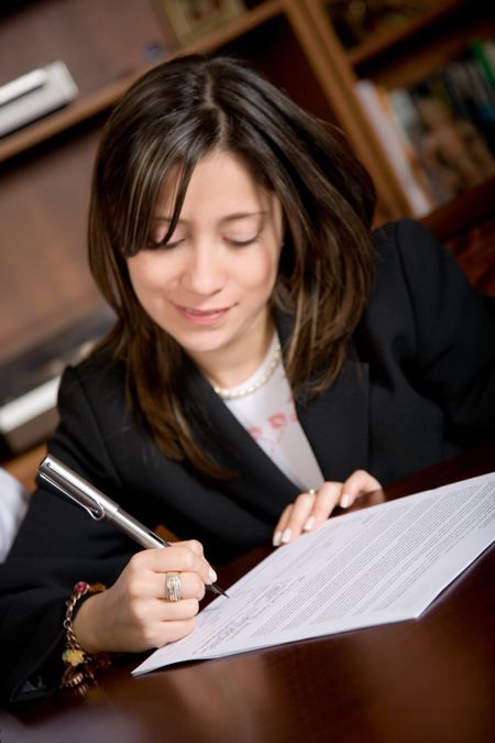 business woman signing a contract in her office - focus is on her right hand therefore text of the letter is not readable