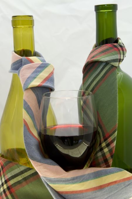 Wine glass with wine nestled by neckties on two wine bottles