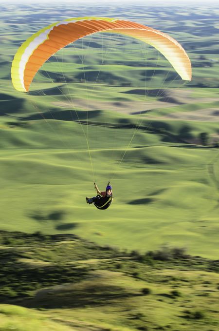 Adult male paraglider over green hills of The Palouse in western Washington, USA