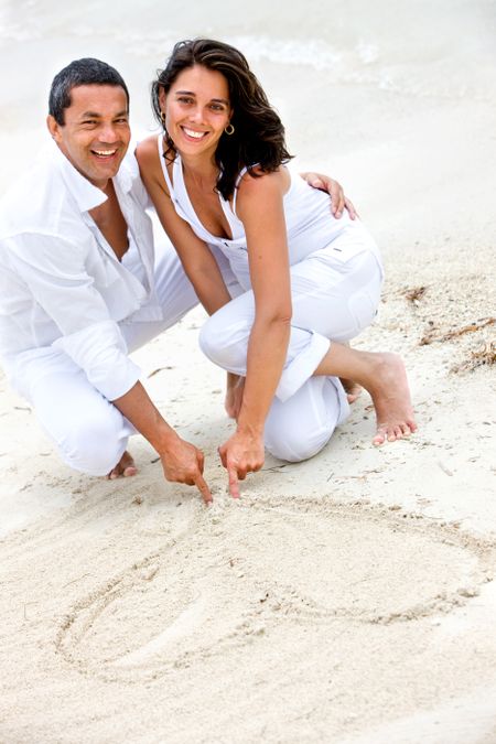 happy couple smiling at the beach drawing a heart on the sand