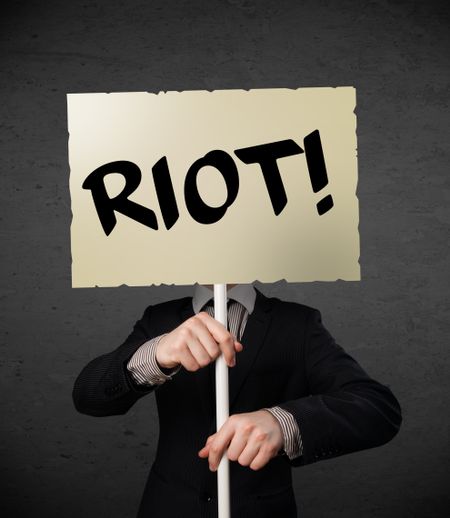 Businessman holding a demonstration board with riot sign in front of his head