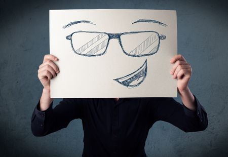 Young businessman holding a paper with smiley face in front of his head