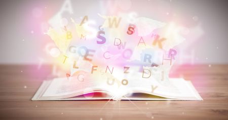 Open book with glowing letters on concrete background. Colorful education concept