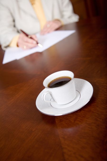cup of espresso on the table while a business woman is signing some papers