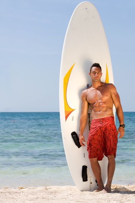 male at the beach standing next to his surfboard