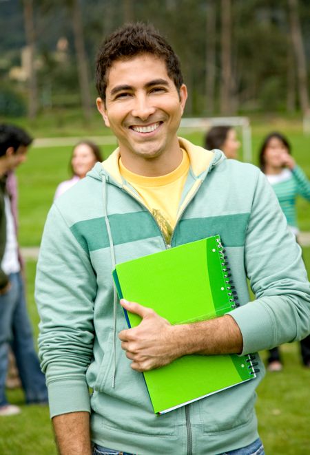 male university student outdoors smiling with a notebook