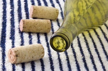 Three corks by wine bottle on striped beach towel