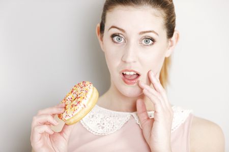Young woman deciding whether to eat an unhealthy doughnut expressing guilt.