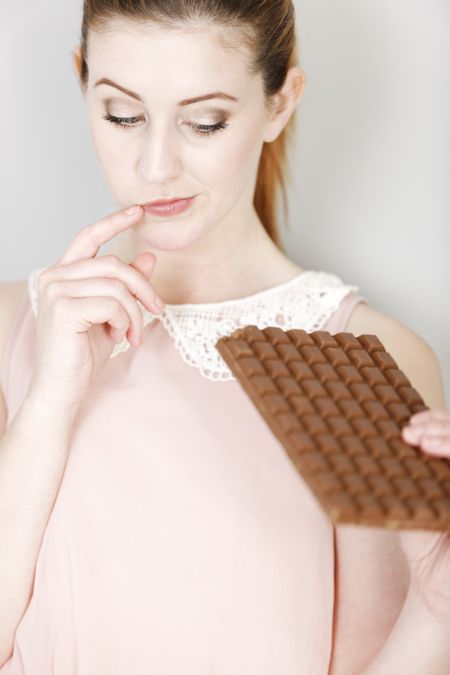 Attractive young woman deciding on whether to eat a piece of chocolate.