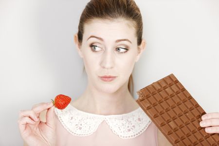 Beautiful young woman choosing to eat chocolate or a fresh strawberry.