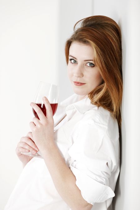 Attractive young woman wearing a white shirt and enjoying a glass of red wine.