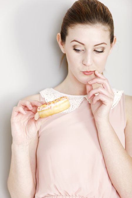 Young woman deciding whether to eat an unhealthy doughnut expressing guilt.