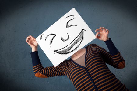 Young woman holding a paper with a drawed smiley face on it in front of her head