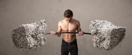 Strong muscular man lifting large rock stone weights