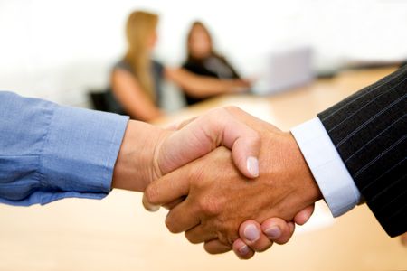 business handshake in an office with team behind