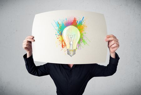 Businessman holding a cardboard with coloured paint splashes and lightbulb in front of his head