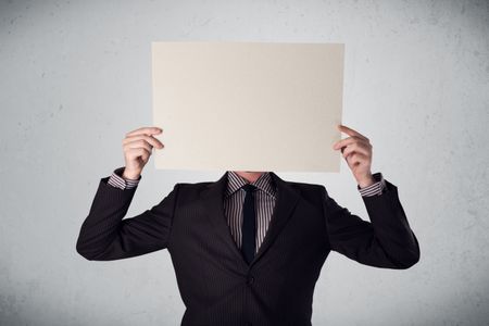 Businessman standing and holding in front of his head a white paper with copy space