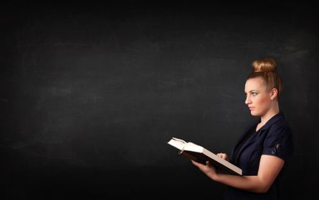 Young lady reading a book in front of a blackboard 