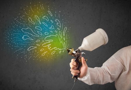 Worker with airbrush gun paints colorful lines and splashes concept