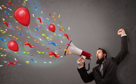 Young guy having fun, shouting into megaphone with balloons and confetti